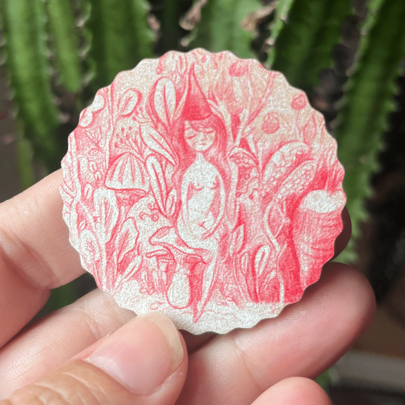 le magnet octobre rose dans ma main. Il représente une jeune femme assise sur un champignon dans une forêt enchantée